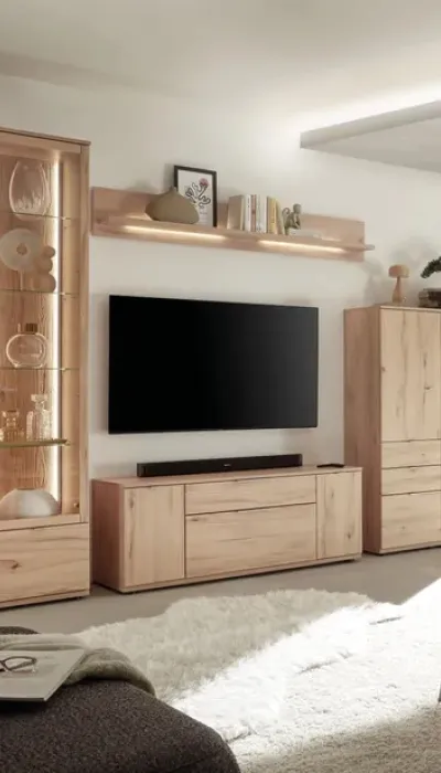 Wohnwand aus heller Eiche mit TV-Board, Vitrine und Hängeregal, kombiniert mit moderner Beleuchtung und dezenten Deko-Elementen für ein helles, gemütliches Wohnzimmerambiente.